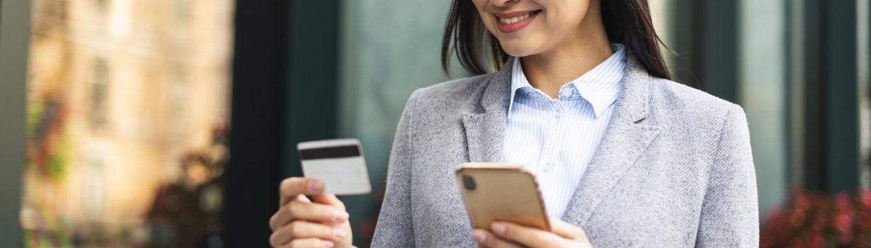 smiley-businesswoman-using-smartphone-credit-card-outdoors